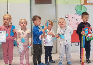 najmłodsze dzieci stoją na sali gimnastycznej z dyplomami i medalami po pasowaniu na przedszkolaka.