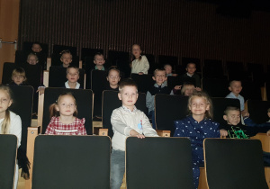 Grupa dzieci siedząca na widowni i słuchająca próby orkiestry.