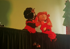 TEATRALNA PACYNKA DIABEŁEK I DZIEWCZYNKA SIEDZĄ NA SCENERII BLISKO SIEBIE I ROZMAWIAJĄ ( KOLOR CZERWIEŃ I CZERŃ )
