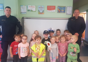 GRUPA POMARAŃCZOWA- dzieci siedzą i stoją, pozując do wspólnego zdjęcia z policjantami.