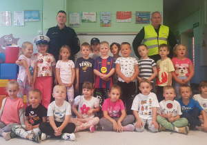 GRUPA ŻÓŁTA - dzieci siedzą i stoją, pozując do wspólnego zdjęcia z policjantami.