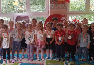 DZIECI Z GRUPY CZERWONEJ POZUJĄ DO ZDJĘCIA W SWOJEJ SALI Z ZAWIESZINYMI MEDALAMI PO UROCZYSTOŚCI DNIA PRZEDSZKOLAKA.